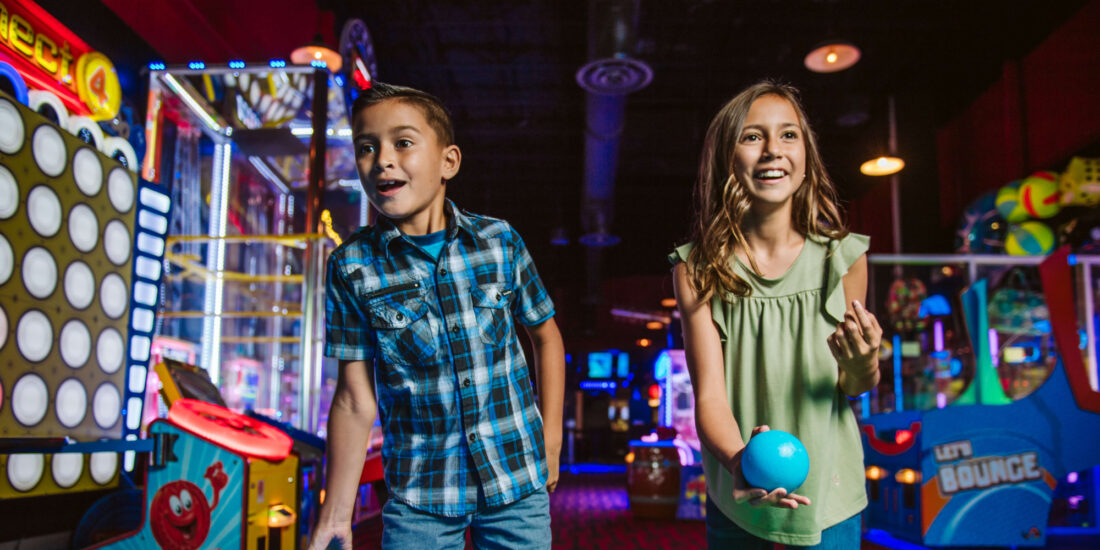 Two kids laugh while playing ski-ball at an Andy B's arcade